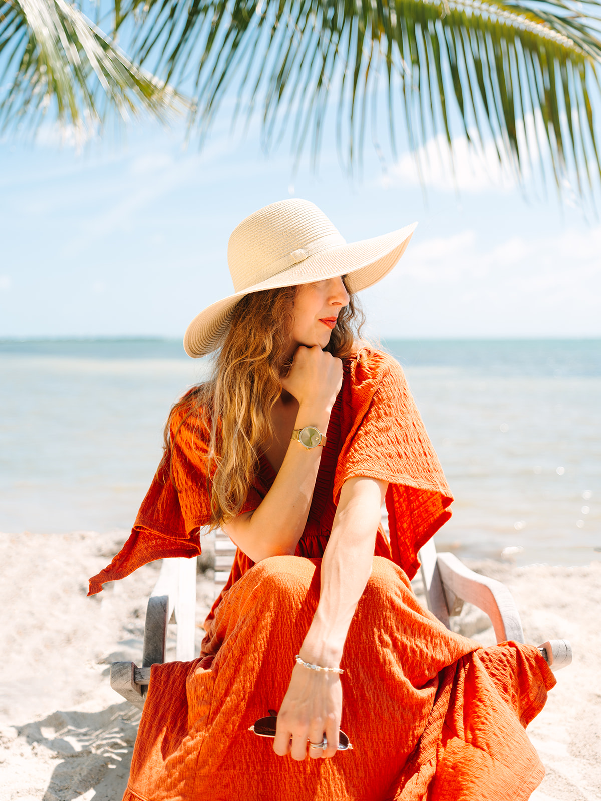 Woman in orange dress wearing sunhat at beach looking in the distance