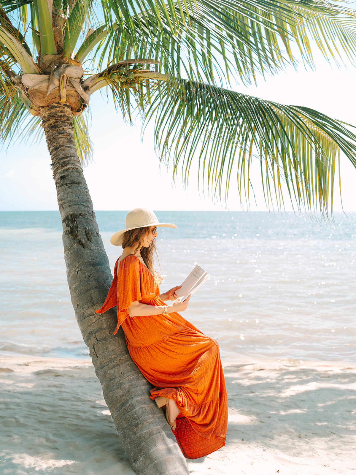 woman in orange dress reading book by the ocean